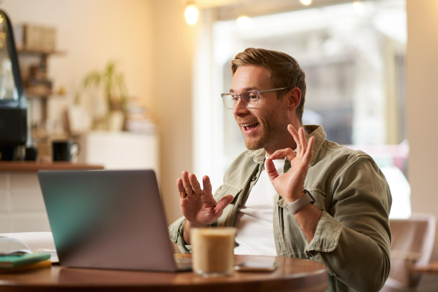 Man attending an online therapy session on a laptop from home, speaking and gesturing during a virtual mental health appointment