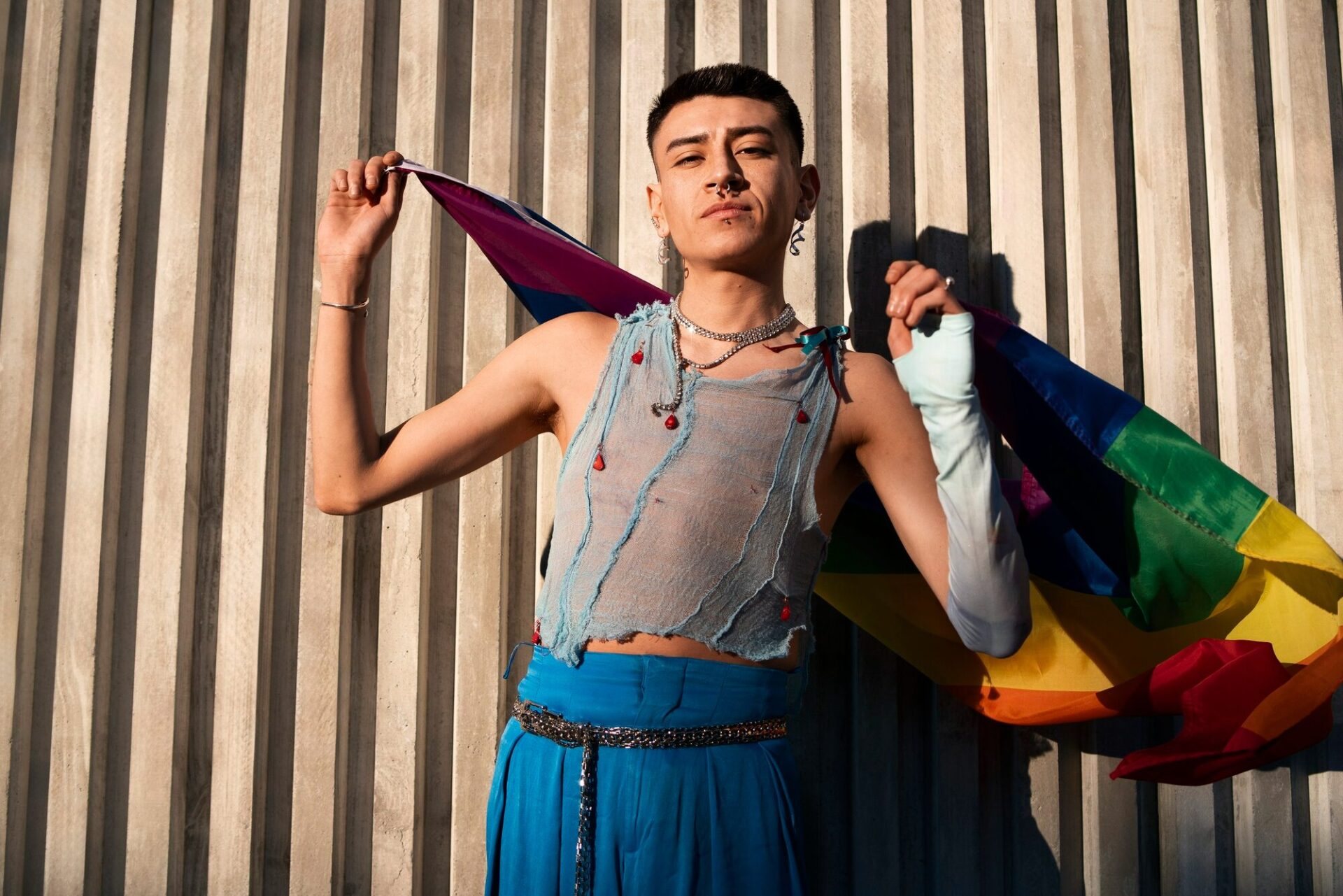 Young person holding a rainbow pride flag outdoors in warm sunlight